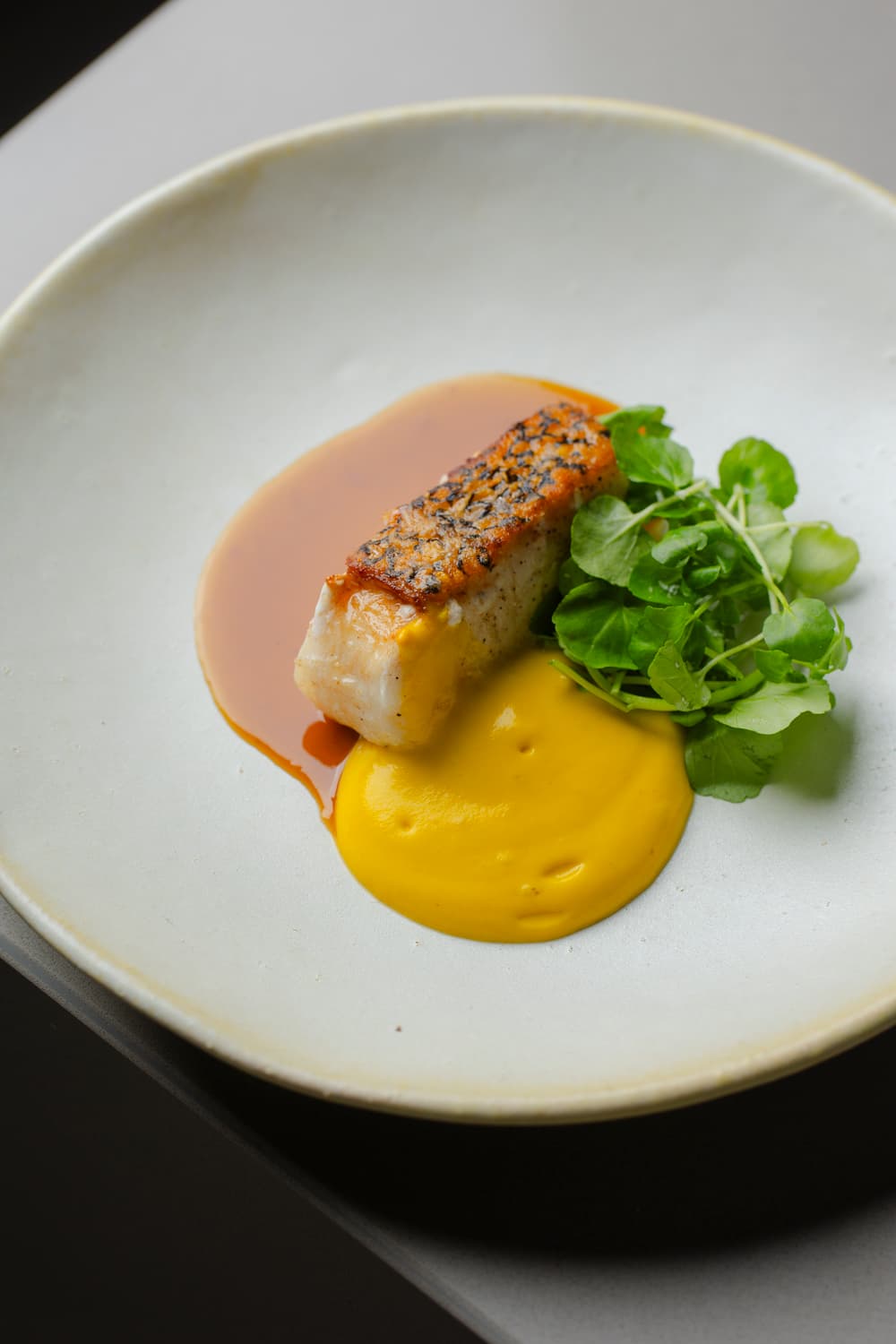 Peixe grelhado com purê amarelo e folhas verdes