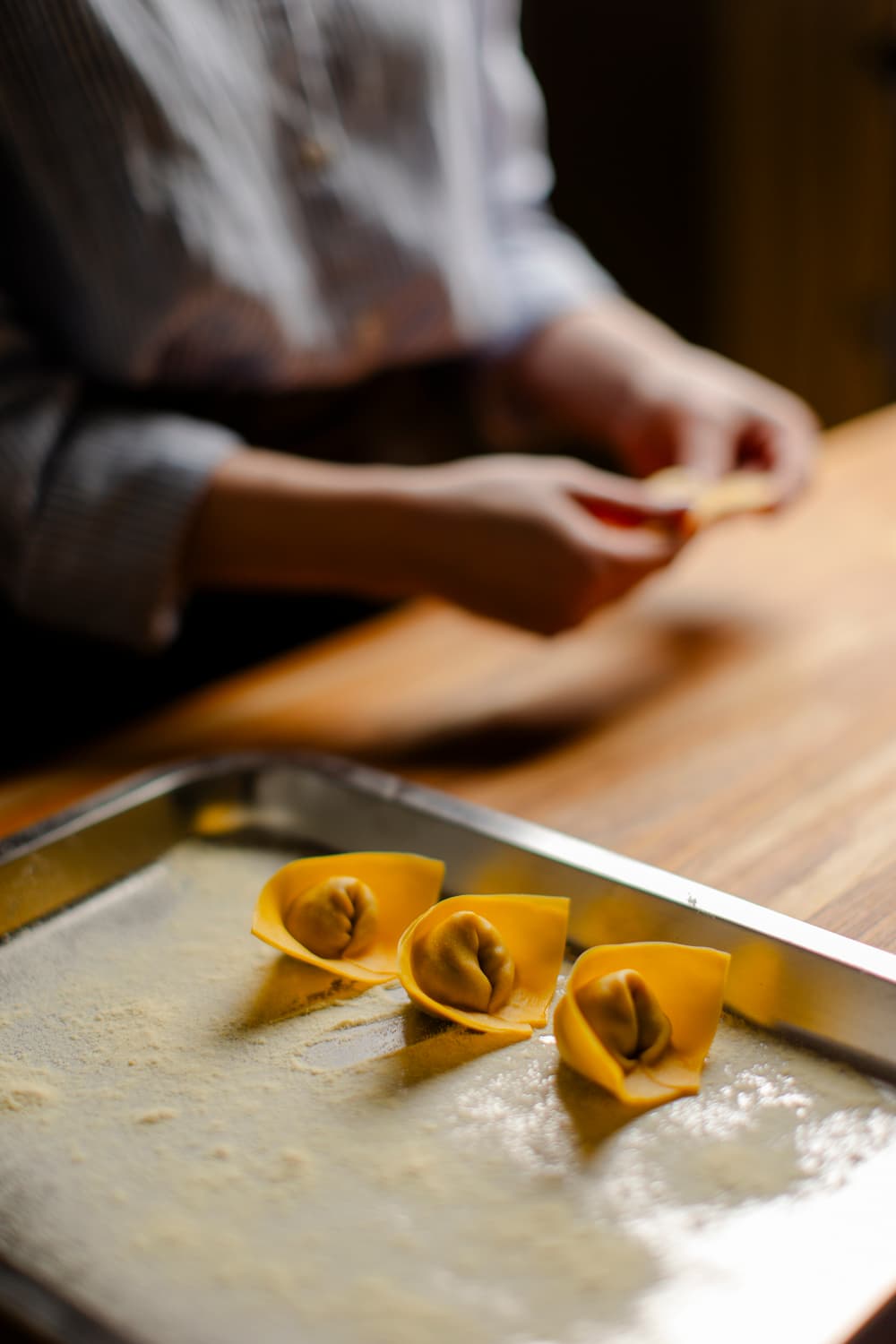 Mãos de Alexia fechando tortelli frescos sobre bandeja